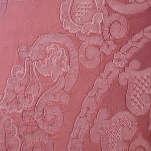 May include: A dusty rose fabric featuring a tonal, raised embroidery pattern of intricate floral and scrolling motifs. The design includes repeating organic shapes, curved lines, and textured grid-like details stitched into the surface.