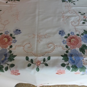 Può includere: Una tovaglia rettangolare bianca con ricami floreali simmetrici nei toni del blu, rosa e verde. Il design presenta intricati motivi a intaglio e dettagliati disegni floreali disposti in due gruppi principali con piccoli tralci.