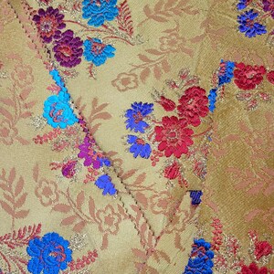 May include: Close-up of a golden fabric with a floral pattern. The design features red, blue, and purple flowers with gold accents. The fabric is likely used for upholstery or decorative purposes.