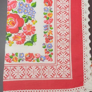 Peut inclure: Un tissu blanc orné d'un imprimé floral aux fleurs rouges, roses et bleues, bordé d'une bande rouge avec des motifs géométriques en point de croix blanc. Le bord est fini par une bordure en dentelle crochetée blanche festonnée.