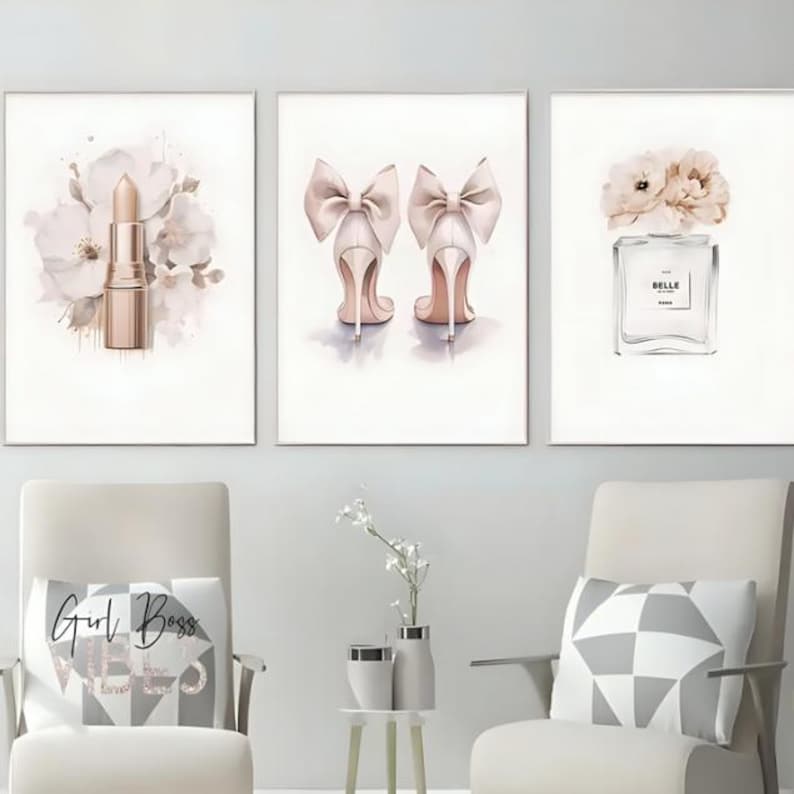 May include: Three framed watercolor prints. One features a gold lipstick with floral accents. Another showcases a pair of high heels with large bows. The third print displays a perfume bottle with floral accents. The prints are displayed above two chairs.
