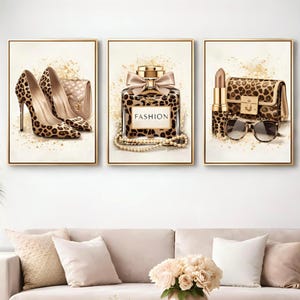 May include: Three framed art prints with fashion illustrations. The prints depict leopard print high heels, a perfume bottle with the word "FASHION", and a handbag, lipstick, and sunglasses, all in a leopard print design.