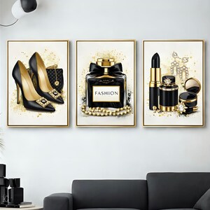 Peut inclure: Trois impressions d'art encadrées représentant des articles de mode. La première montre des talons hauts noirs, un sac à main et des accents dorés. La seconde représente un flacon de parfum avec un nœud noir et le mot "FASHION". La troisième affiche rouge à lèvres, bijoux et maquillage.