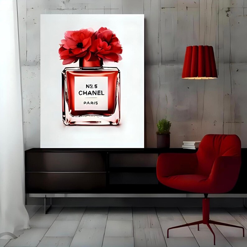 May include: A framed art print featuring a red perfume bottle with the text "N&deg;5 CHANEL PARIS" and topped with red flowers. The artwork is displayed above a black cabinet, with a red chair and lamp in the background.