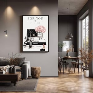 May include: A framed wall art print featuring the text FOR YOU WITH LOVE, a black quilted handbag, a glass vase with pink peonies, stacked books labeled CHANEL, a black and white striped ribbon, and a lipstick tube on a white background.