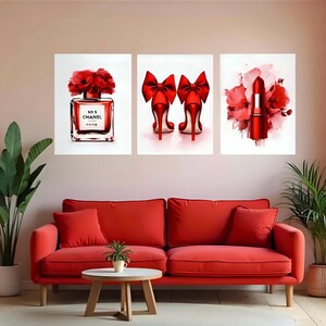 May include: Three framed art prints featuring a perfume bottle, high heels, and lipstick in shades of red. The perfume bottle is labeled "N&deg;5 CHANEL PARIS". The high heels have large red bows. The lipstick is surrounded by red flowers.