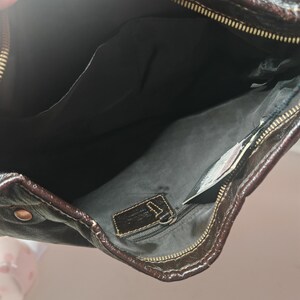 Peut inclure: Un sac &agrave; main en cuir marron fonc&eacute; avec une fermeture &eacute;clair sur le dessus et des d&eacute;tails dor&eacute;s. L'int&eacute;rieur est doubl&eacute; de tissu noir et comprend une poche zipp&eacute;e avec une &eacute;tiquette en cuir ainsi qu'une poche ouverte pour le rangement.