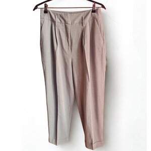 Peut inclure: Pantalon taille haute de couleur marron clair, suspendu à un cintre marron foncé. Le pantalon a un devant plissé, des poches latérales et un ourlet retroussé. Le tissu semble être un matériau tissé léger.