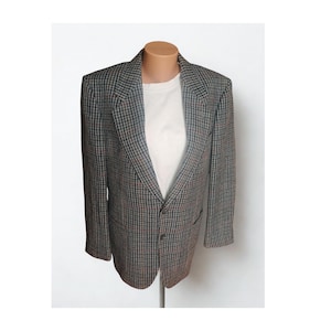 May include: A houndstooth blazer in grey, brown, and red, displayed on a mannequin. The jacket features a classic notched lapel, two front pockets, and a two-button closure. A white t-shirt is visible underneath.