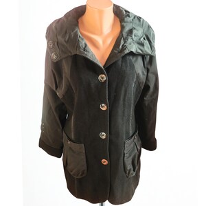 May include: A black jacket with a distinctive design. It has a large collar, button fastenings, and two front pockets. The jacket is displayed on a mannequin against a white background.