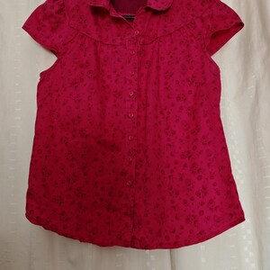 May include: A pink button-up shirt with a floral pattern and short sleeves.