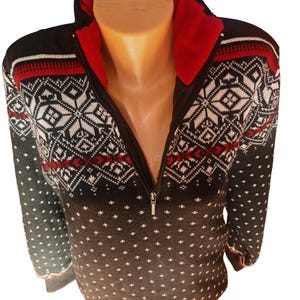 May include: A black and white patterned sweater with a red fleece-lined collar. The sweater features a half-zip closure and a snowflake design on the upper chest. The lower portion of the sweater has a dotted pattern.