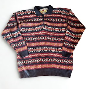 May include: A long-sleeved sweater with a navy blue collar and cuffs. The sweater features a geometric pattern in red, white, and orange on a navy blue background. The collar has a small tag with text.