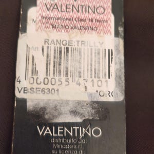 Peut inclure: Une &eacute;tiquette produit rectangulaire noire avec le logo Valentino en haut et en bas. Le centre comprend une &eacute;tiquette blanche avec le texte International Class 18 Items, Mario Valentino, Range: Trilly, un code-barres et le code VBSE6301.