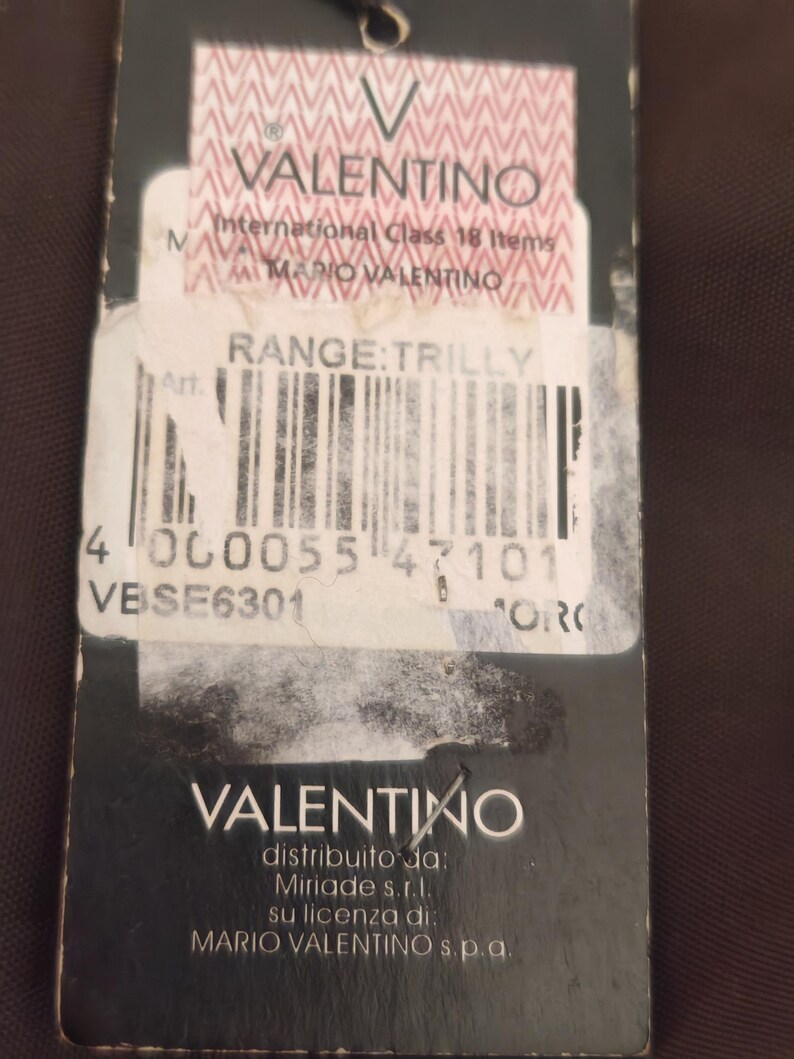 Peut inclure: Une &eacute;tiquette produit rectangulaire noire avec le logo Valentino en haut et en bas. Le centre comprend une &eacute;tiquette blanche avec le texte International Class 18 Items, Mario Valentino, Range: Trilly, un code-barres et le code VBSE6301.