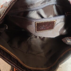 Peut inclure: L'int&eacute;rieur d'un sac &agrave; main marron fonc&eacute; avec une doublure en tissu marron fonc&eacute;, une fermeture &eacute;clair sur le dessus et une poche int&eacute;rieure zipp&eacute;e. Un &eacute;cusson en cuir marron fonc&eacute; est cousu sur la doublure avec du texte en relief.