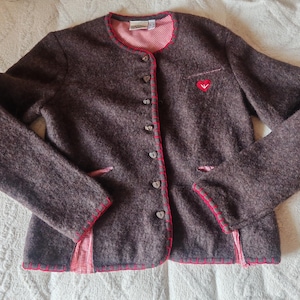 May include: A brown wool jacket with a red heart detail and red trim. The jacket has a round neckline, button closures, and two front pockets. The interior lining is red and white gingham.