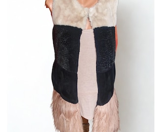 May include: A faux fur vest in a colour block design. The vest features a cream-coloured upper section, a black centre, and a blush-coloured lower section with fringe. The vest is displayed on a mannequin.