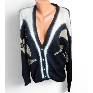 Peut inclure: Un cardigan vintage noir, blanc et beige avec un col en V et une fermeture boutonnée. Le pull présente un motif géométrique avec des ornements floraux et en forme d'étoiles. Le pull à manches longues est présenté sur un mannequin.