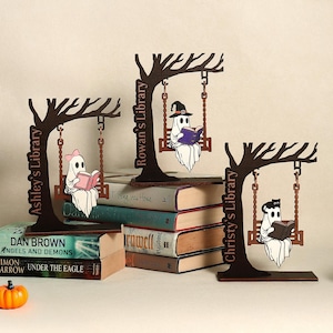 May include: Three wooden Halloween-themed bookends featuring ghost figures reading books while swinging from tree branches. Each bookend has a different name on the tree trunk: Ashley's Library, Rowan's Library, and Christy's Library.