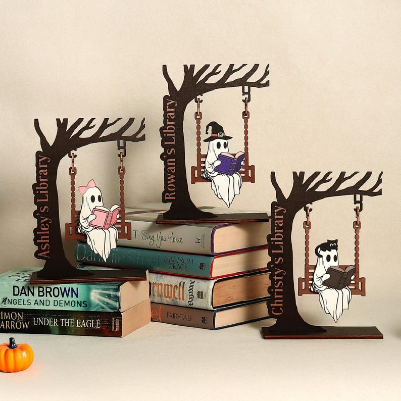 May include: Three wooden Halloween-themed bookends featuring ghost figures reading books while swinging from tree branches. Each bookend has a different name on the tree trunk: Ashley's Library, Rowan's Library, and Christy's Library.