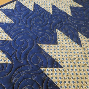 K&ouml;nnte beinhalten: Ein blauer und cremefarbener gesteppter Tischl&auml;ufer mit einem wirbelnden Muster und einem Design aus kleinen Sternen.