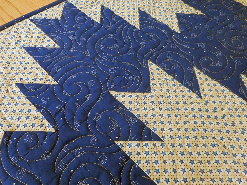 K&ouml;nnte beinhalten: Ein blauer und cremefarbener gesteppter Tischl&auml;ufer mit einem wirbelnden Muster und einem Design aus kleinen Sternen.