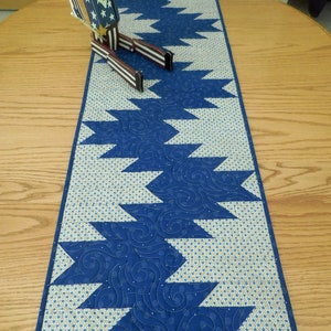 K&ouml;nnte beinhalten: Ein blauer und wei&szlig;er Tischl&auml;ufer mit geometrischem Muster. Der L&auml;ufer ist gesteppt mit einem wirbelnden Design. Eine patriotische Holzfigur sitzt auf dem L&auml;ufer.