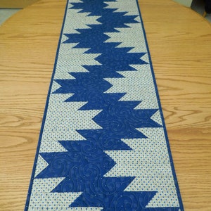 K&ouml;nnte beinhalten: Ein blauer und wei&szlig;er Tischl&auml;ufer mit geometrischem Muster. Der L&auml;ufer ist aus Stoff und hat ein gestepptes Design.