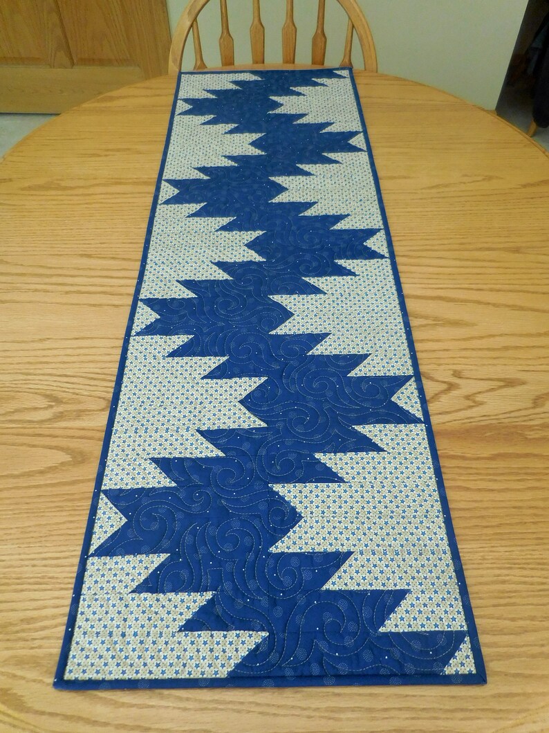K&ouml;nnte beinhalten: Ein blauer und wei&szlig;er Tischl&auml;ufer mit geometrischem Muster. Der L&auml;ufer ist aus Stoff und hat ein gestepptes Design.