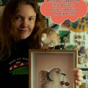 May include: A light-colored dove perched on a wooden frame containing a watercolor illustration of a dove holding two cherries in its beak. A coral-colored speech bubble above contains the text: When you support my small business you're supporting my big dream.