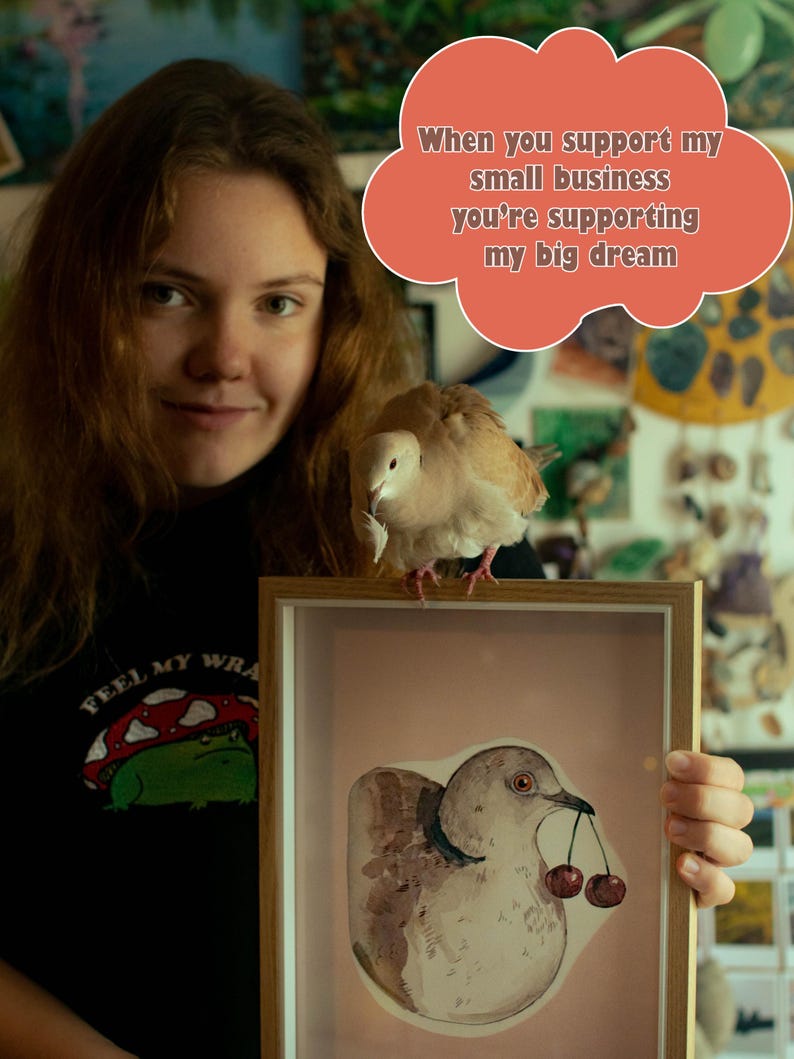 May include: A light-colored dove perched on a wooden frame containing a watercolor illustration of a dove holding two cherries in its beak. A coral-colored speech bubble above contains the text: When you support my small business you're supporting my big dream.