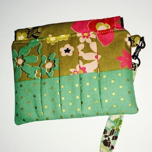 May include: A green and brown fabric clutch with a floral print and gold polka dots. The clutch has a short strap.