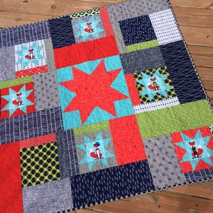 May include: A red, gray, blue, and green patchwork quilt with a star pattern and fox illustrations.