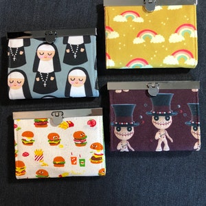 May include: Four different small zippered pouches with various colorful patterns. The pouches are made of fabric and have a metal zipper closure. The patterns include a nun design, a rainbow design, a burger design, and a voodoo doll design.
