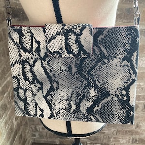 May include: A black and white snakeskin patterned crossbody bag with a flap closure and a silver chain strap.