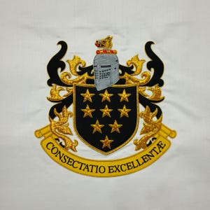 May include: Embroidered crest on white fabric. The crest features a black shield with nine gold stars, a silver helmet, and gold filigree. A gold banner at the bottom reads "CONSECTATIO EXCELLENT&AElig;". The design is detailed with black and gold thread.