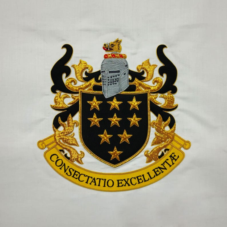 May include: Embroidered crest on white fabric. The crest features a black shield with nine gold stars, a silver helmet, and gold filigree. A gold banner at the bottom reads "CONSECTATIO EXCELLENT&AElig;". The design is detailed with black and gold thread.