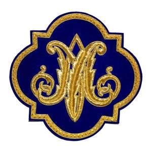 May include: A blue embroidered patch with a gold border and a gold monogram. The monogram features ornate, intertwined letters. The patch has a quatrefoil shape, with a detailed gold border that complements the central design.