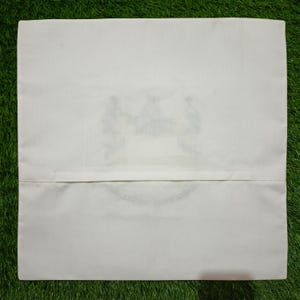 May include: Off-white cushion cover with a concealed zip closure. The cushion cover features a subtle design in the centre, with a light green and blue colour scheme. The cover is made of a soft, smooth fabric.