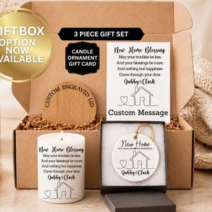 Puede incluir: Un juego de regalo de tres piezas en una caja de cart&oacute;n, que incluye una vela, un adorno y una tarjeta. La vela y la tarjeta presentan el texto "New Home Blessing" y una ilustraci&oacute;n de una casa.