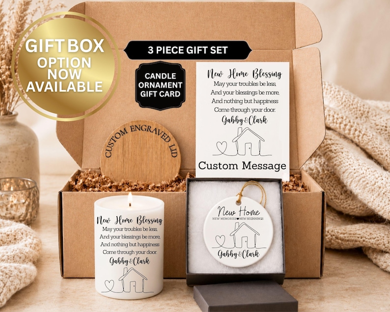 Puede incluir: Un juego de regalo de tres piezas en una caja de cart&oacute;n, que incluye una vela, un adorno y una tarjeta. La vela y la tarjeta presentan el texto "New Home Blessing" y una ilustraci&oacute;n de una casa.