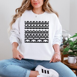 May include: White sweatshirt with a black geometric pattern. The design features horizontal bands of various shapes, including rectangles, triangles, and stylized elements. The sweatshirt is a casual, long-sleeved garment.