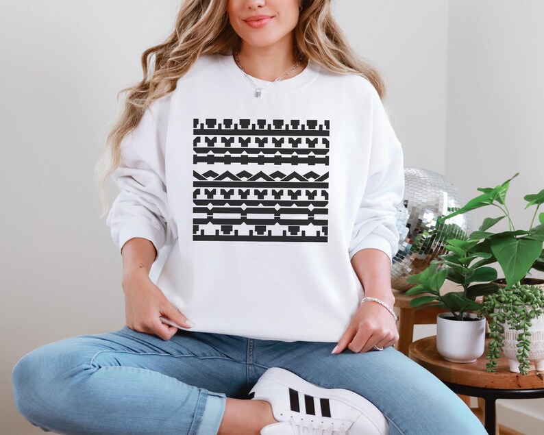 May include: White sweatshirt with a black geometric pattern. The design features horizontal bands of various shapes, including rectangles, triangles, and stylized elements. The sweatshirt is a casual, long-sleeved garment.