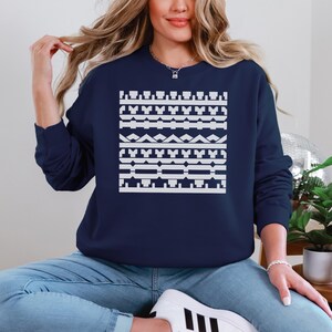 May include: A navy blue sweatshirt featuring a white geometric pattern across the chest. The design consists of various shapes and lines, creating a symmetrical and visually appealing design. The sweatshirt is a casual, comfortable garment.