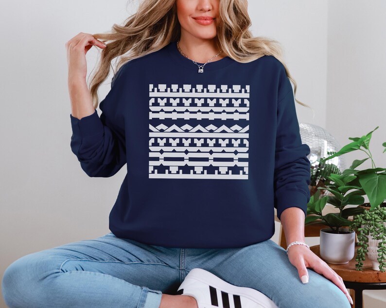 May include: A navy blue sweatshirt featuring a white geometric pattern across the chest. The design consists of various shapes and lines, creating a symmetrical and visually appealing design. The sweatshirt is a casual, comfortable garment.