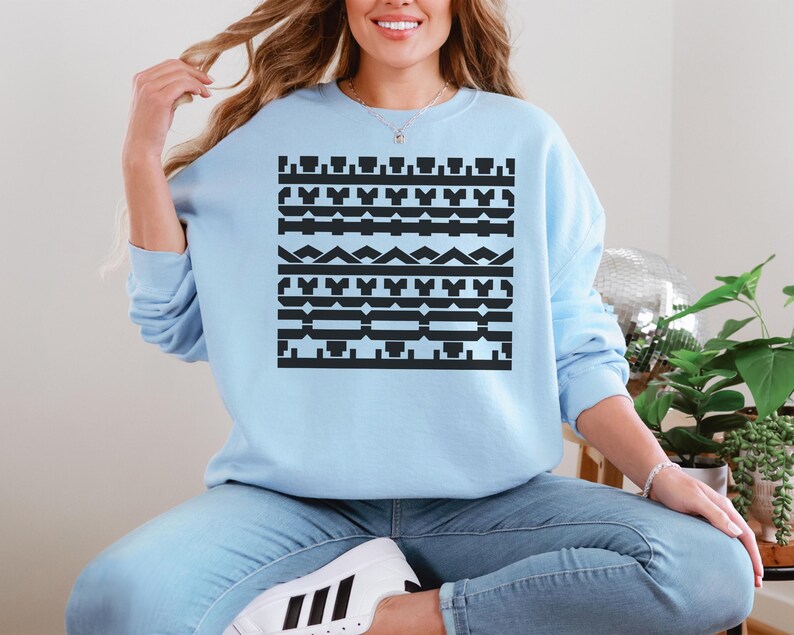 May include: A light blue sweatshirt with a black geometric pattern. The pattern consists of various shapes, including rectangles, triangles, and other abstract designs. The sweatshirt is long-sleeved and has a crew neck.