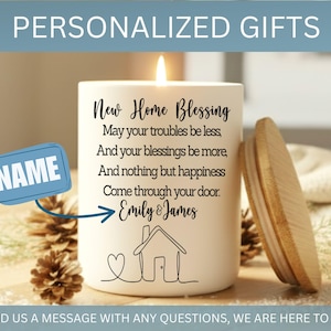Puede incluir: Una vela blanca con tapa de madera, con el texto "New Home Blessing" y una ilustraci&oacute;n de una casa. La vela incluye un espacio para un nombre y est&aacute; rodeada de pi&ntilde;as. La vela est&aacute; encendida.