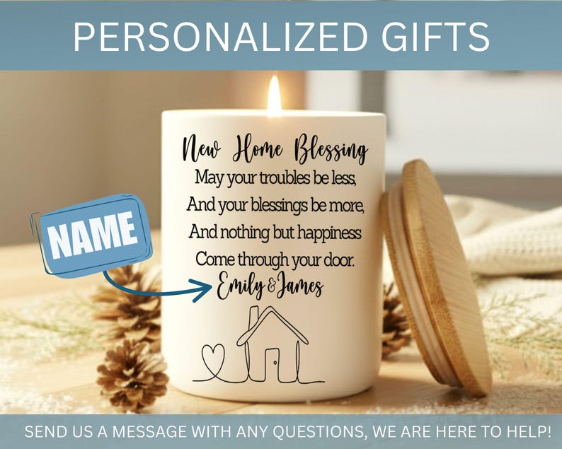 Puede incluir: Una vela blanca con tapa de madera, con el texto "New Home Blessing" y una ilustraci&oacute;n de una casa. La vela incluye un espacio para un nombre y est&aacute; rodeada de pi&ntilde;as. La vela est&aacute; encendida.