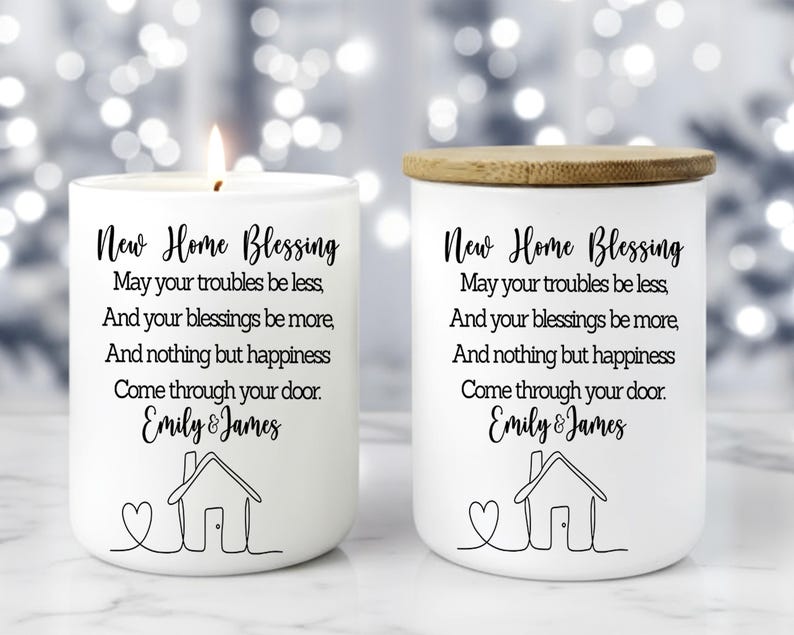 Puede incluir: Dos velas de cer&aacute;mica blanca con tapas de madera. Una vela est&aacute; encendida. Cada vela tiene el texto "New Home Blessing" y un mensaje personalizado con una ilustraci&oacute;n de una casa. Un regalo de inauguraci&oacute;n.